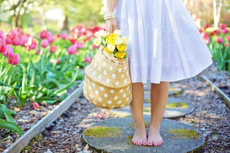 A handmade May Day basket hanging on a white picket fence with spring flowers spilling over the edge