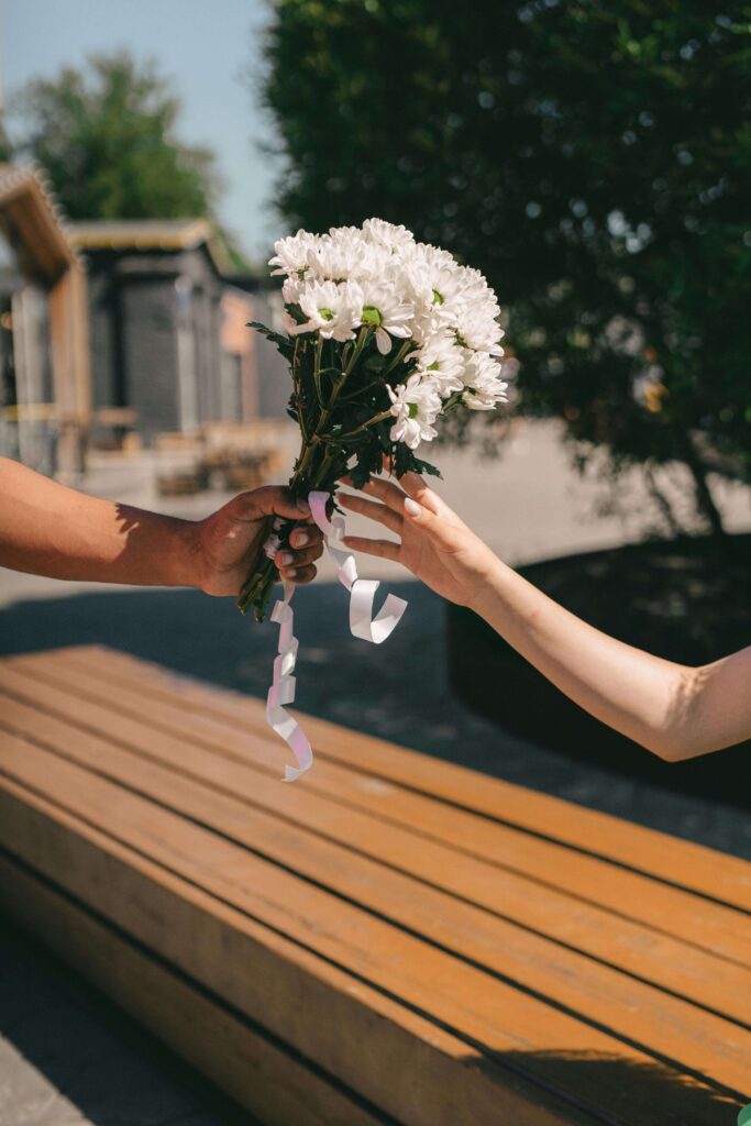A hand delivering a small flower basket to a doorstep on a sunny spring day