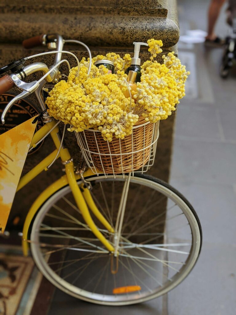 A hand delivering a small flower basket to a doorstep on a sunny spring day