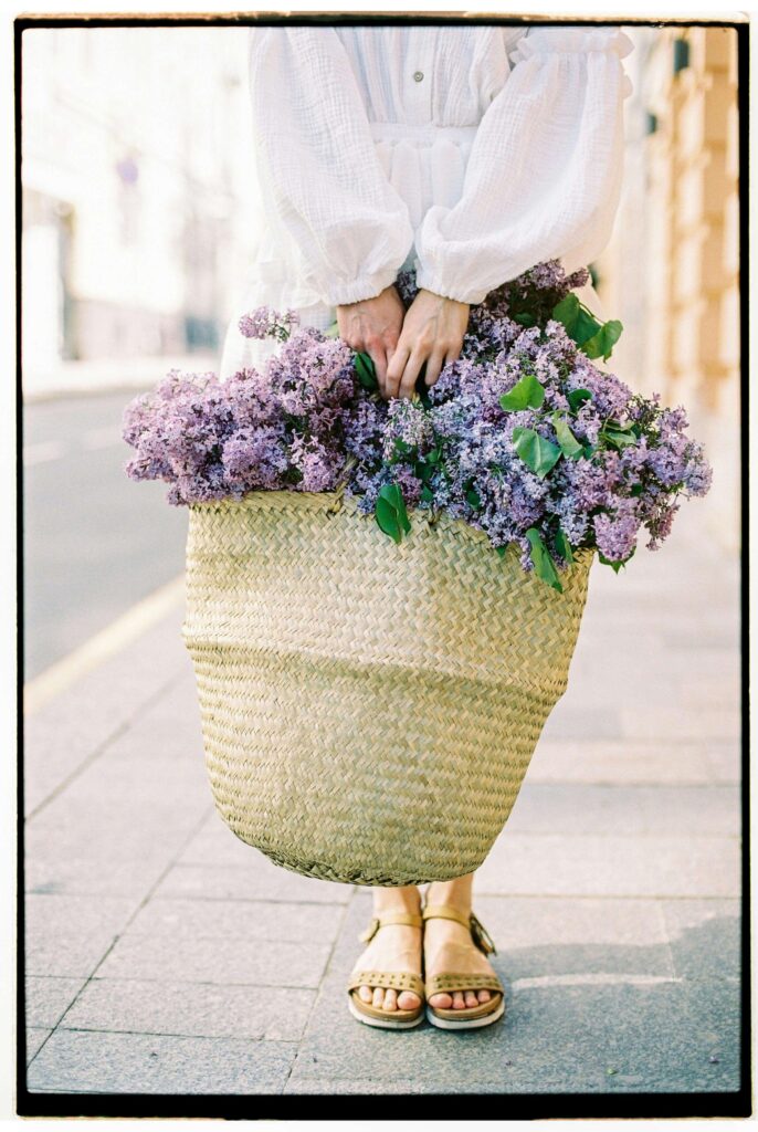 A May Day basket with lilacs, maple candies, and fresh herbs arranged on a linen cloth
